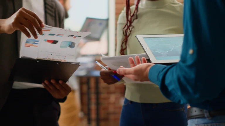 diverse colleagues working business partnership with charts information data research planning group presentation analyzing graphs report with coworkers files tablet close up