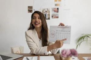mulher de cabelos castanhos longos e roupa formal branca em um escritório sentada na cadeira e segurando um calendário indicando a escala 4x3
