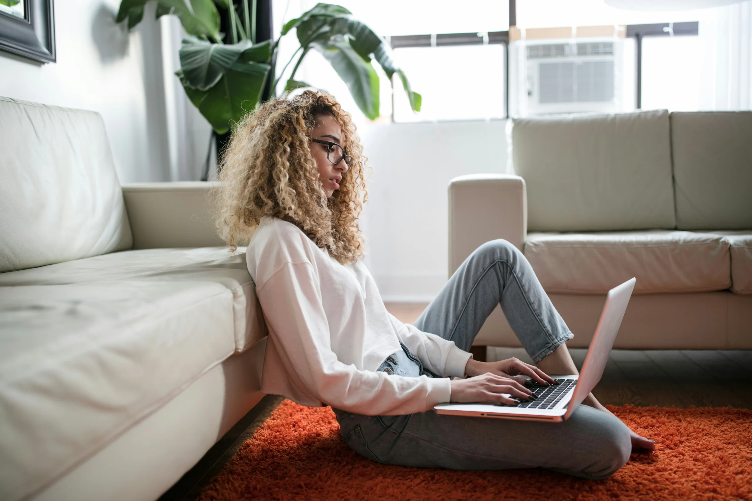 woman sitting on floor and leaning on couch using laptop scaled mulher da geração z sentada no chão e encostada no sofá usando notebook