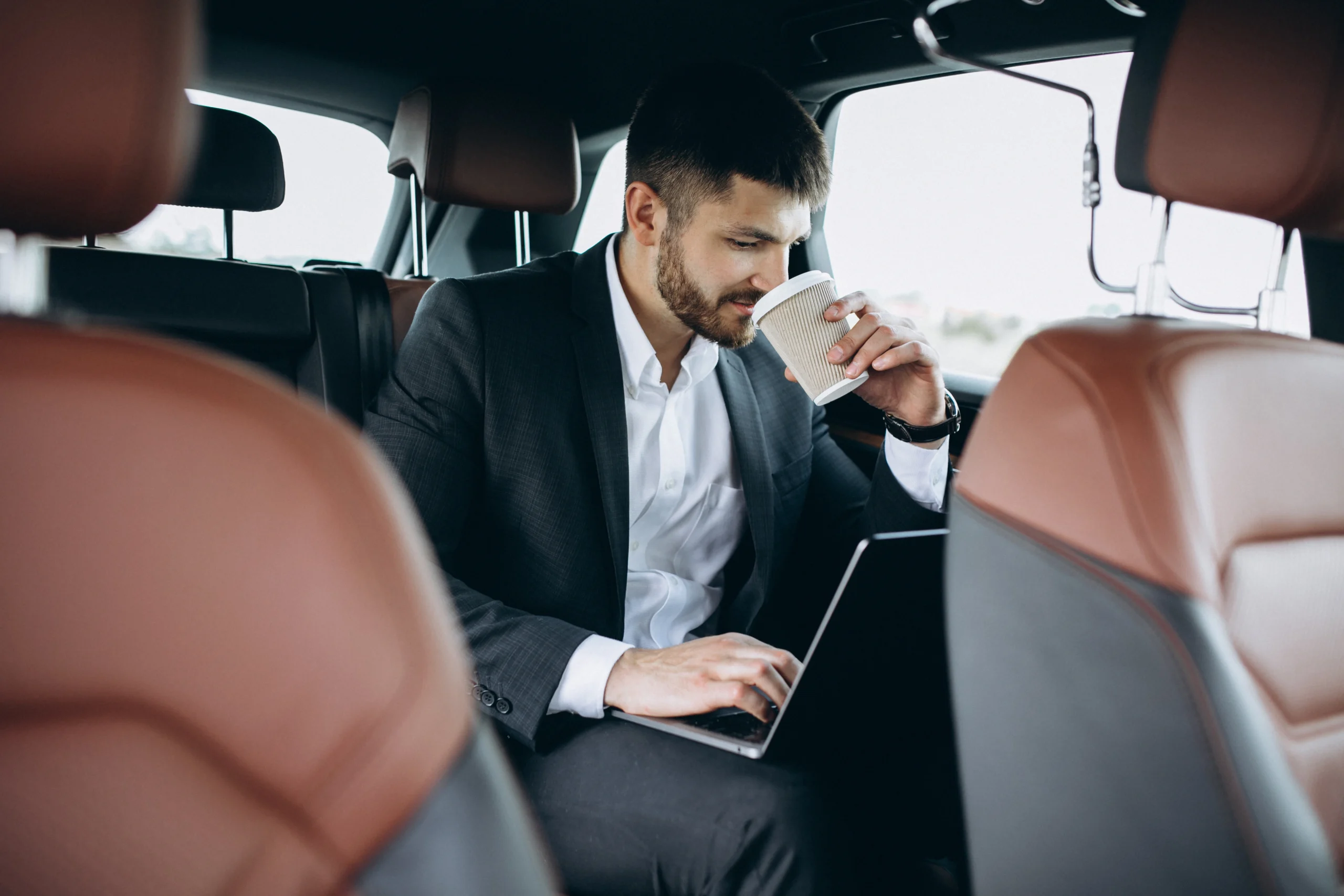 homem de negocios bonito trabalhando em um computador no carro scaled homem de negocios bonito trabalhando em um computador no carro scaled