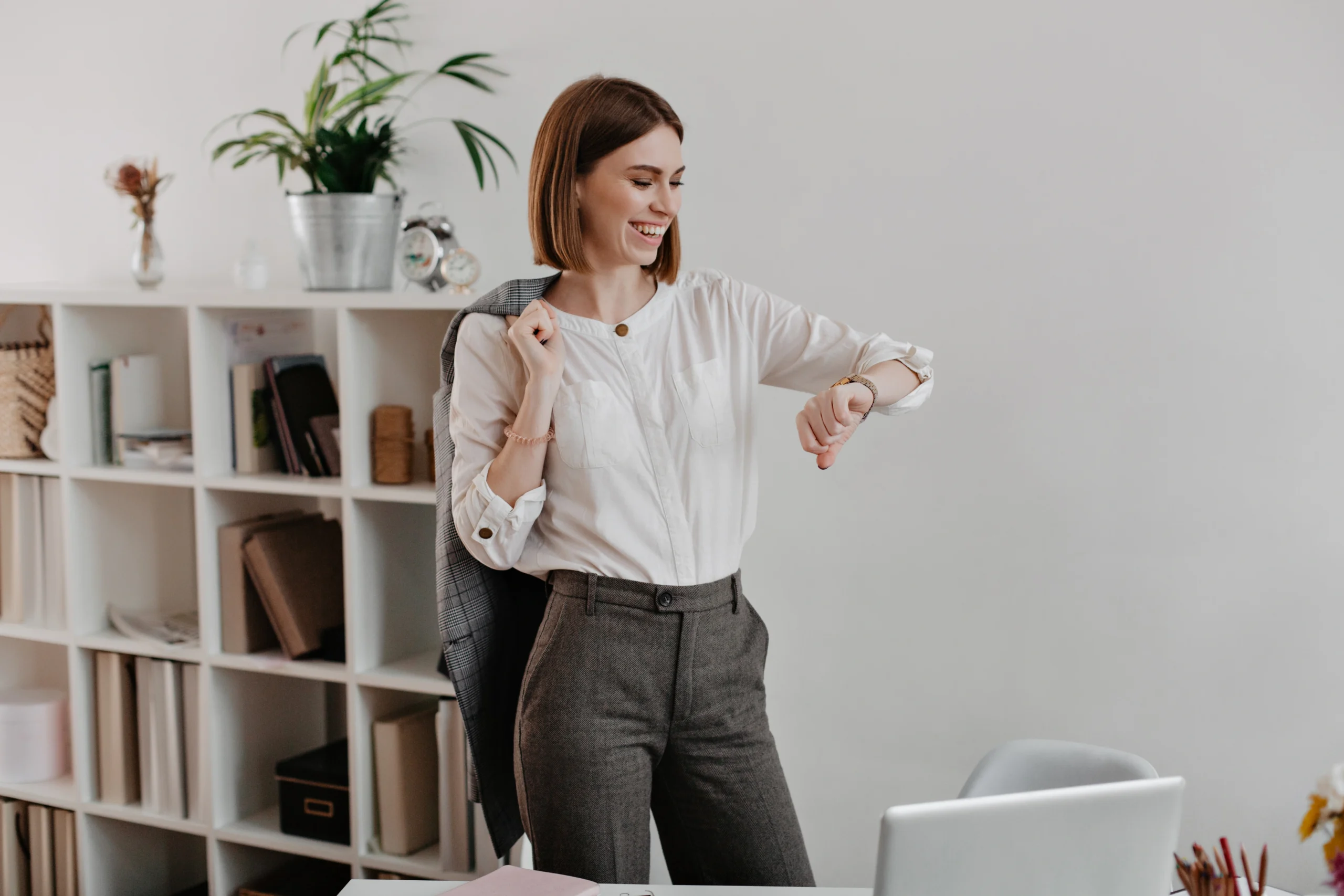 laughing business woman white blouse gray pants is looking wrist watch standing against office furniture scaled laughing business woman white blouse gray pants is looking wrist watch standing against office furniture scaled