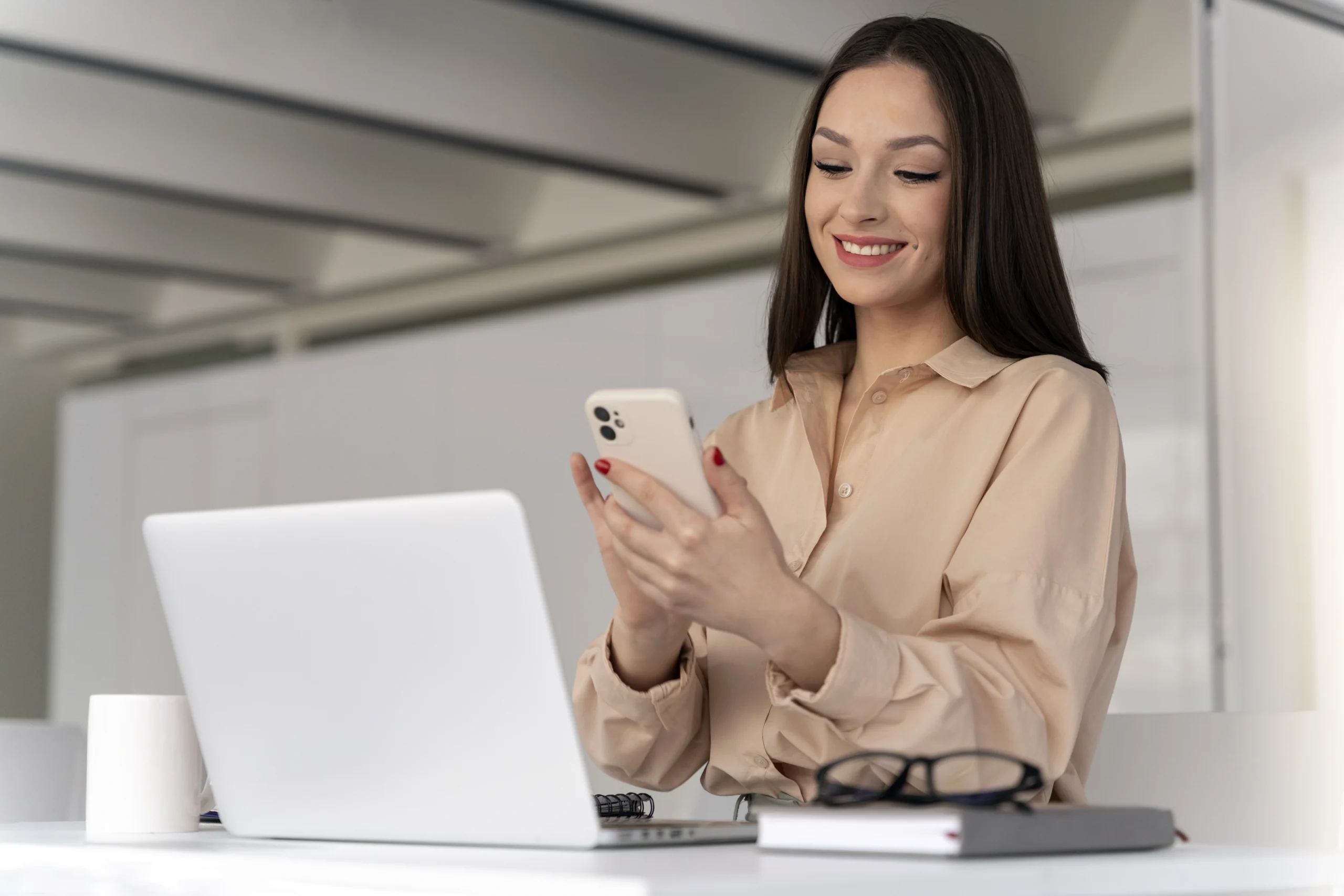 mulher de negocios jovem trabalhando em sua mesa com um smartphone scaled mulher de negocios jovem trabalhando em sua mesa com um smartphone scaled