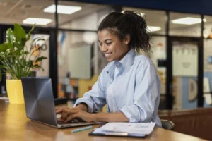 mulher negra de cabelo amarrado usando roupa social e sentada mexendo no computador exercendo suas habilidades em alta
