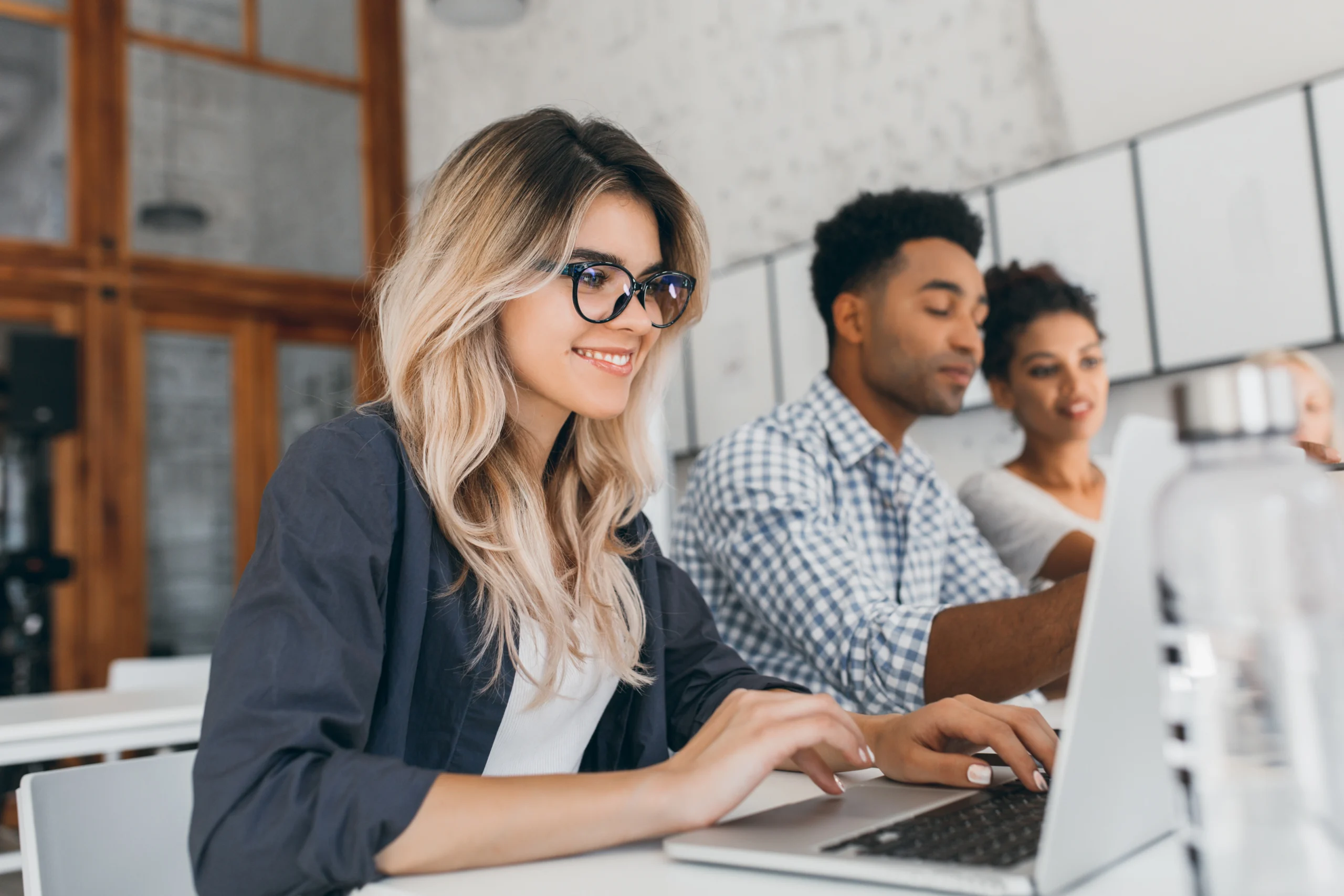beautiful curly female freelancer with cute manicure using laptop smiling indoor portrait blonde secretary sitting beside african coworker blue shirt scaled beautiful curly female freelancer with cute manicure using laptop smiling indoor portrait blonde secretary sitting beside african coworker blue shirt scaled