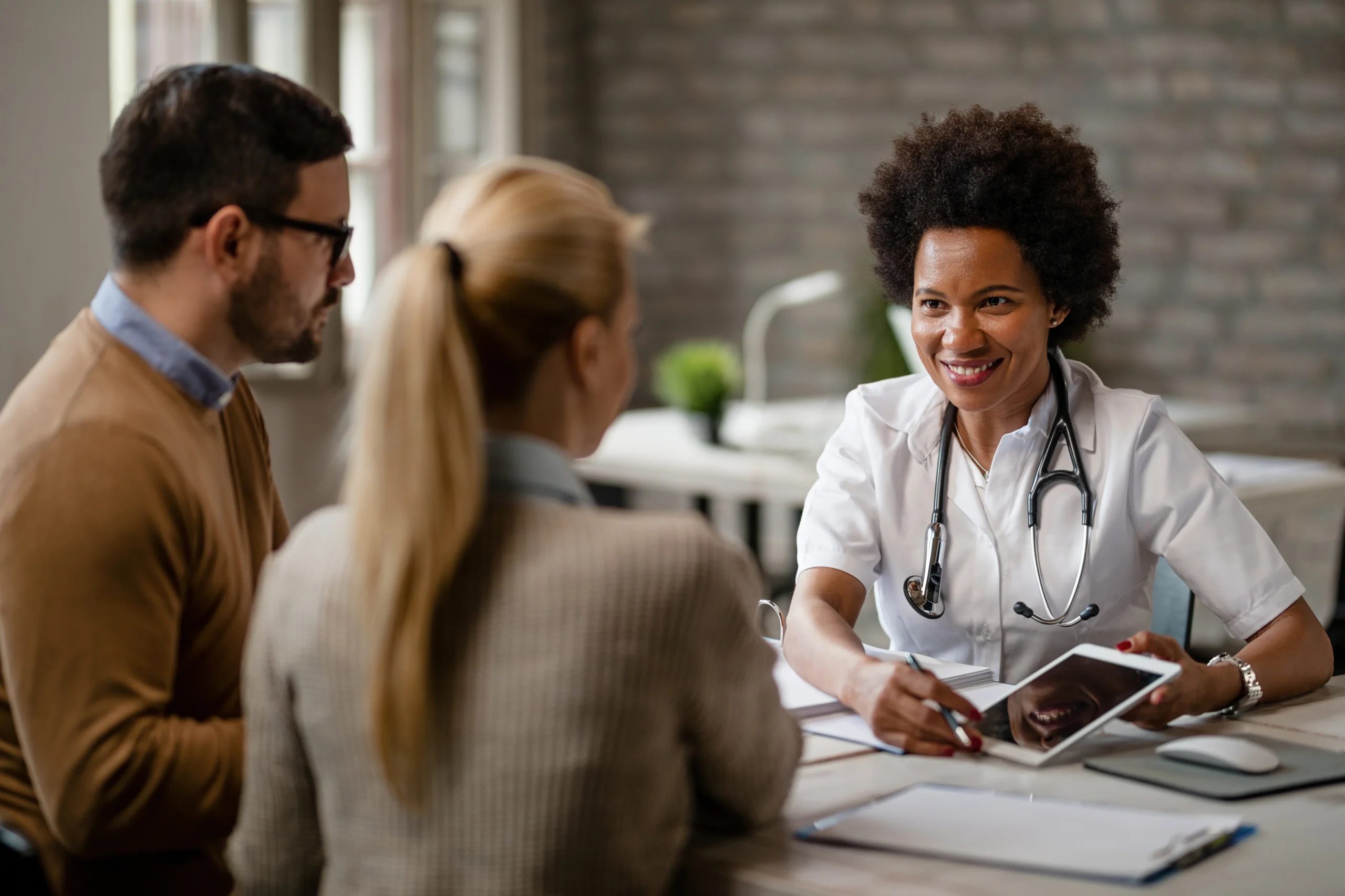feliz medica negra conversando com um casal e mostrando os resultados dos exames medicos em um touchpad durante as consultas na clinica scaled feliz medica negra conversando com um casal e mostrando os resultados dos exames medicos em um touchpad durante as consultas na clinica scaled