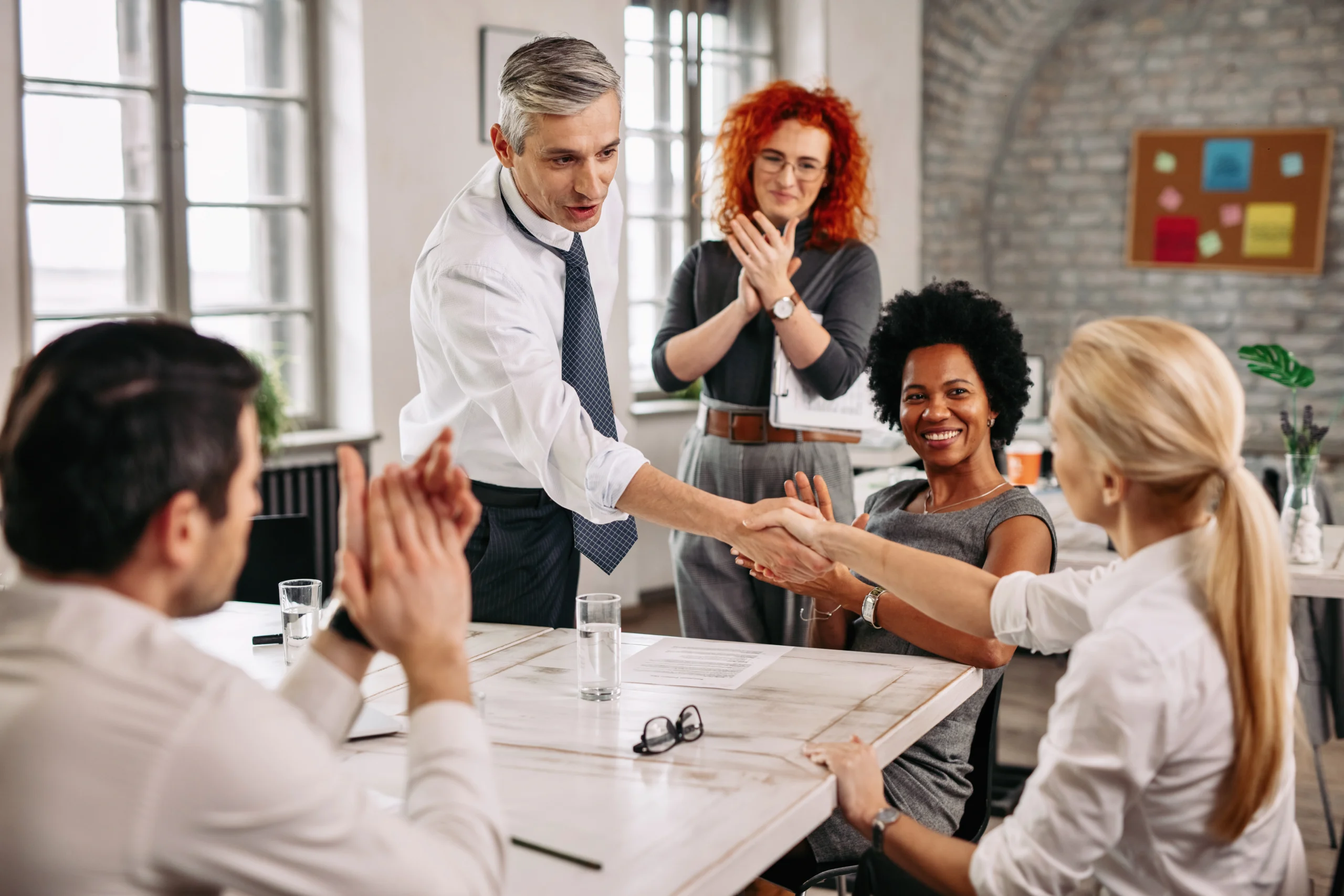 two happy business people shaking hands meeting while other colleagues are applauding them office scaled two happy business people shaking hands meeting while other colleagues are applauding them office scaled