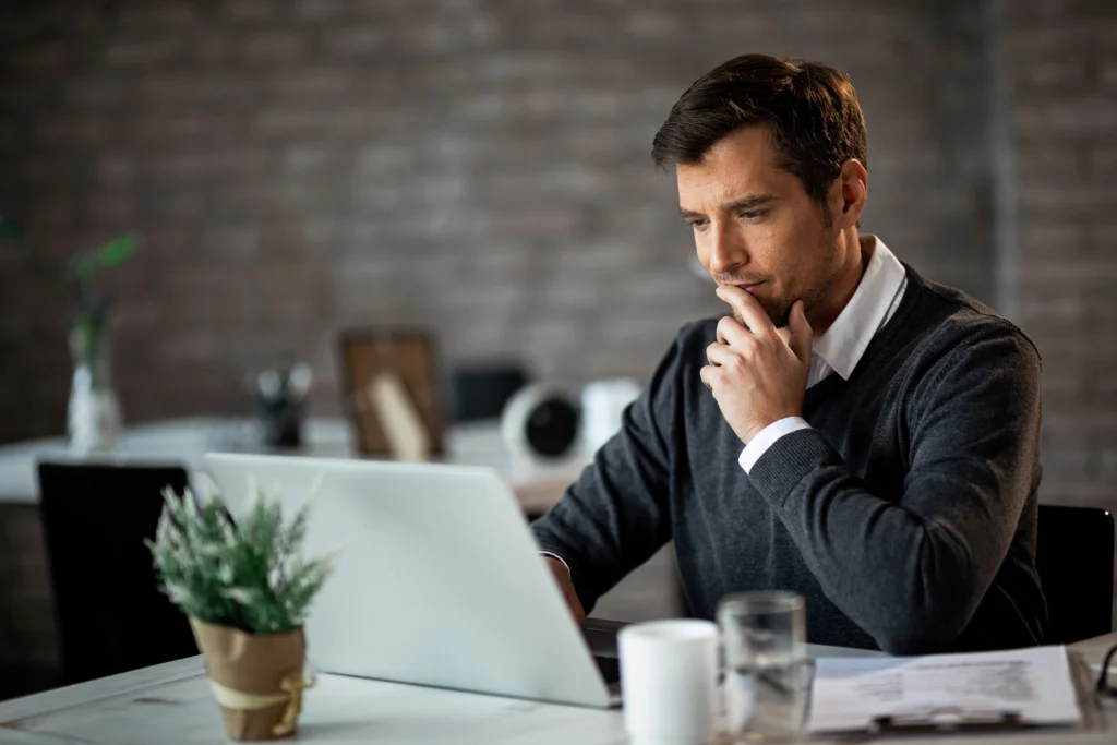 smiling businessman using laptop contemplating while working his desk office smiling businessman using laptop contemplating while working his desk office