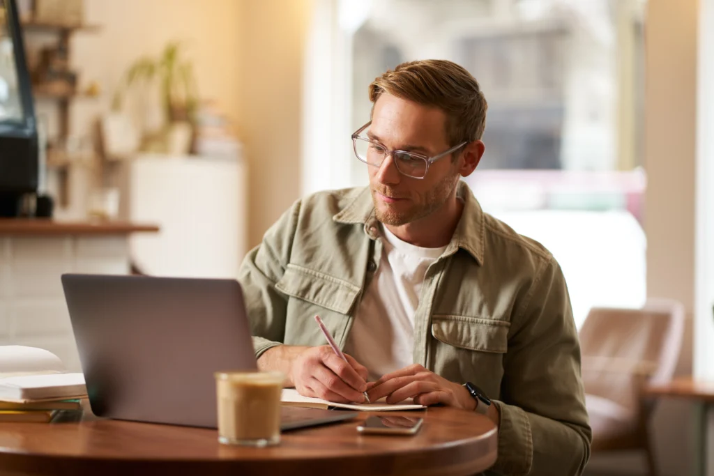 image focused young man glasses sitting cafe making notes studying attending online course image focused young man glasses sitting cafe making notes studying attending online course